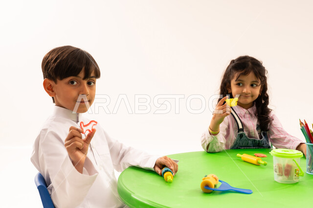 Doing fun and entertaining skills and activities, developing artistic skills through shaping, educational sessions and classes in Saudi kindergartens, a portrait of Saudi Arabian Gulf students playing with clay and colored paste, developing mental and intellectual abilities, white background