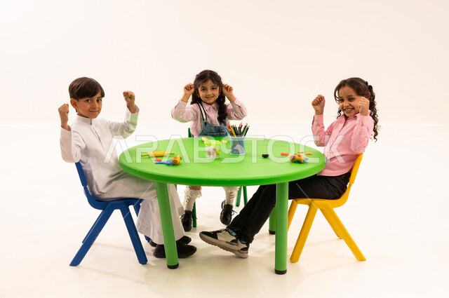 Doing fun and entertaining skills and activities, developing artistic skills through shaping, educational sessions and classes in Saudi kindergartens, a portrait of Saudi Arabian Gulf students playing with clay and colored paste, developing mental and intellectual abilities, white background