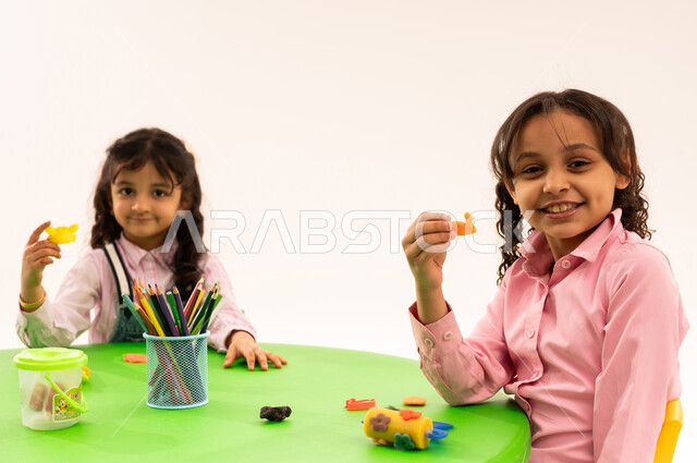 Doing fun and entertaining skills and activities, developing artistic skills through shaping, educational sessions and classes in Saudi kindergartens, a portrait of Saudi Arabian Gulf students playing with clay and colored paste, developing mental and intellectual abilities, white background