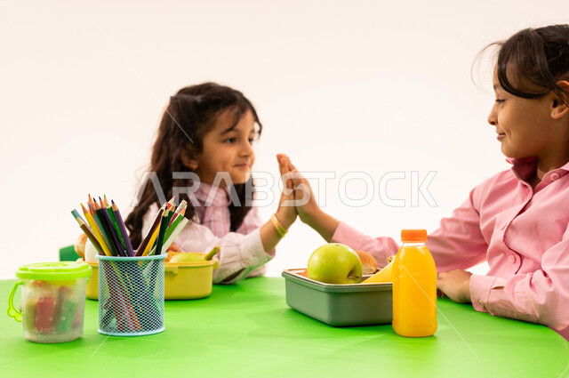 Eating during free time, basics of healthy eating, recess in kindergarten, portrait of Saudi Arabian Gulf Arab boys in casual clothes eating healthy food during school recess in a kindergarten in Saudi Arabia, white background