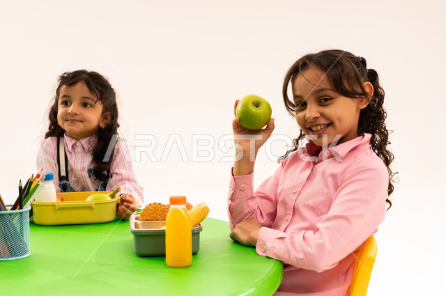 Foundations of healthy eating, leisure time and eating, recess in kindergarten, portrait of Saudi Arabian Gulf Arab boys in casual clothes eating healthy food during school recess in a kindergarten in Saudi Arabia, white background