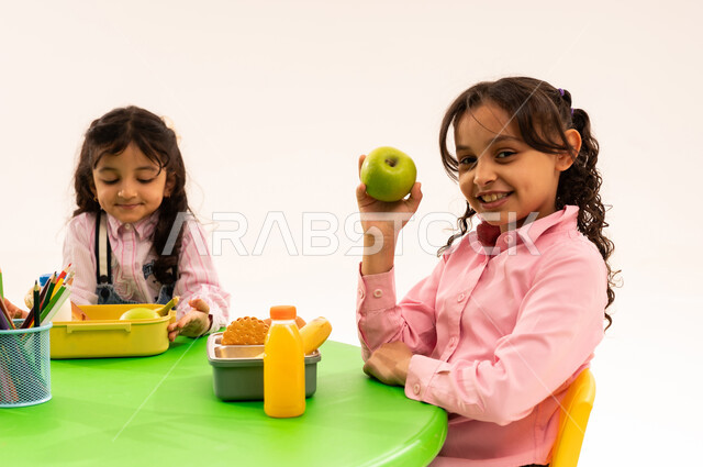Eating during free time, basics of healthy eating, recess in kindergarten, portrait of Saudi Arabian Gulf Arab boys in casual clothes eating healthy food during school recess in a kindergarten in Saudi Arabia, white background