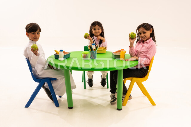 Foundations of healthy eating, leisure time and eating, recess in kindergarten, portrait of Saudi Arabian Gulf Arab boys in casual clothes eating healthy food during school recess in a kindergarten in Saudi Arabia, white background