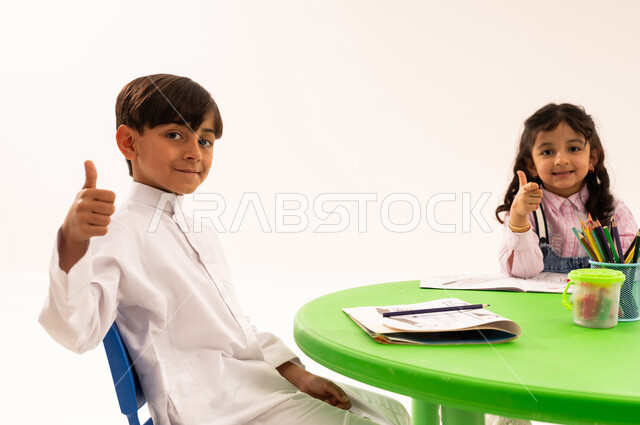 رفع اصبع الابهام بتعابير الاعجاب والقبول، تقوية المهارات الفنية بالرسم والتلوين، الجلسات والحصص التعليمية في الروضات السعودية، بورتريه لطلاب عرب خليجيين سعوديين يقومون بتلوين الرسومات بايماءات السرور، القيام بالمهارات والأنشطة المسلية، خلفية بيضاء