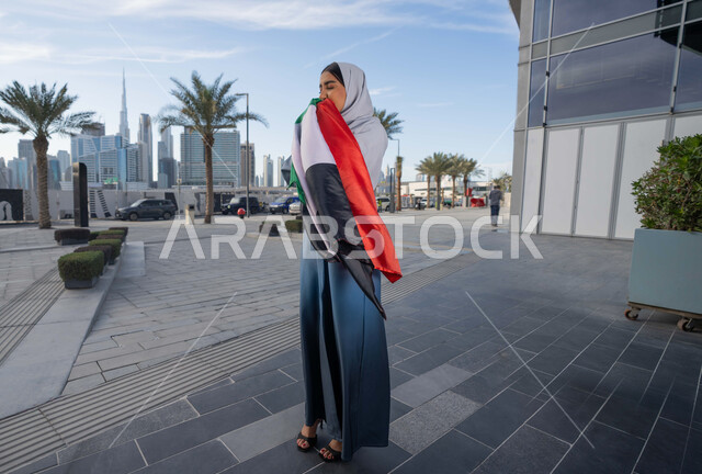 اليوم الوطني الإماراتي 2 ديسمبر،  الاحتفال بذكرى استقلال دولة الإمارات العربية المتحدة، امراة عربية خليجية اماراتية ترتدي العباءة والحجاب تقبل علم الإمارات في النهار، التجول في الشوارع بايماءات السعادة والفخر والاعتزاز، مفهوم حب الوطن والانتماء اليه