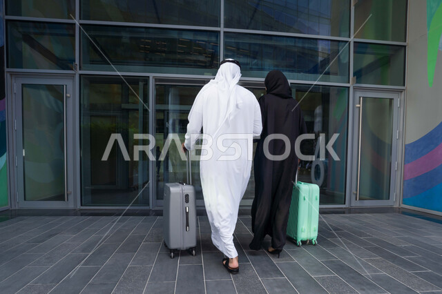 زوجان عربيان خليجيان اماراتيان يجران حقائب الامتعة امام الفندق، تعابير وايماءات السعادة والسرور، عائلة تقضي وقت ممتع، الاستعداد للسفر في جولة سياحية، قضاء رحلة صيفية مسلية، مفهوم السياحة في إجازة الصيف