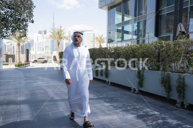 انتهاء وقت الدوام الرسمي، رجل عربي خليجي اماراتي يرتدي الغترة والكندورة التقليدية يخرج من الشركة بايماءات الثقة بالنفس، الحضور المبكر والنشاط الصباحي للعمل، بيئة العمل المريحة في شركات الامارات العربية المتحدة، التجول في الهواء الطلق