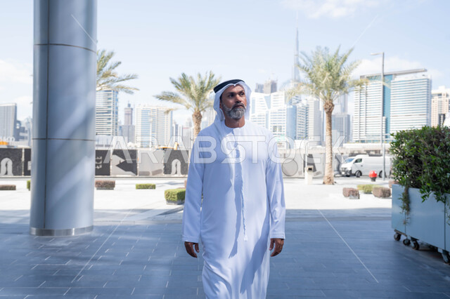 Comfortable work environment in UAE companies, walking in the fresh air, the end of official working hours, an Emirati Gulf Arab man wearing the traditional ghutra and kandura leaving the company with gestures of self-confidence, early arrival and morning activity for work