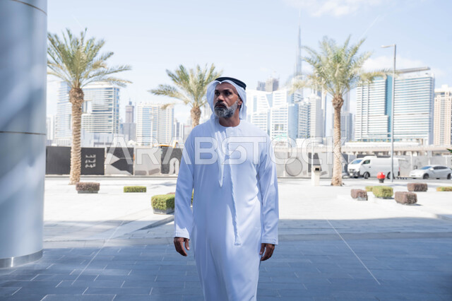 بيئة العمل المريحة في شركات الامارات العربية المتحدة، التجول في الهواء الطلق، انتهاء وقت الدوام الرسمي، رجل عربي خليجي اماراتي يرتدي الغترة والكندورة التقليدية يخرج من الشركة بايماءات الثقة بالنفس، الحضور المبكر والنشاط الصباحي للعمل