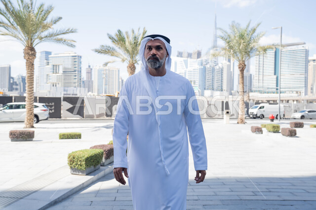 انتهاء وقت الدوام الرسمي، رجل عربي خليجي اماراتي يرتدي الغترة والكندورة التقليدية يخرج من الشركة بايماءات الثقة بالنفس، الحضور المبكر والنشاط الصباحي للعمل، بيئة العمل المريحة في شركات الامارات العربية المتحدة، التجول في الهواء الطلق