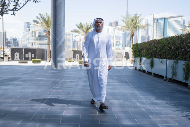الحضور المبكر والنشاط الصباحي للعمل، بيئة العمل المريحة في شركات الامارات العربية المتحدة، التجول في الهواء الطلق، انتهاء وقت الدوام الرسمي، رجل عربي خليجي اماراتي يرتدي الغترة والكندورة التقليدية يخرج من الشركة بايماءات الثقة بالنفس