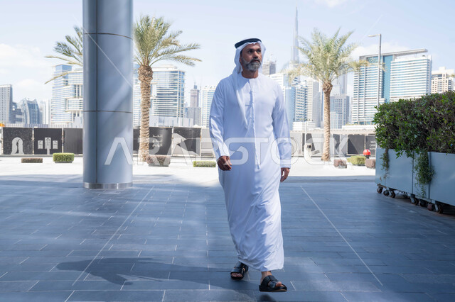 Early arrival and morning activity at work, comfortable working environment in UAE companies, outdoor walks, end of official working hours, an Emirati Gulf Arab man wearing the traditional ghutra and kandura leaving the company with gestures of self-confidence