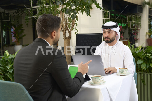Business development and strategies, success and goal achievement. An Emirati Gulf Arab businessman in a business meeting with a new client wearing a formal suit, using a laptop. A close-up of an Emirati young man wearing a white kandora and ghutra, completing projects and tasks in a café.