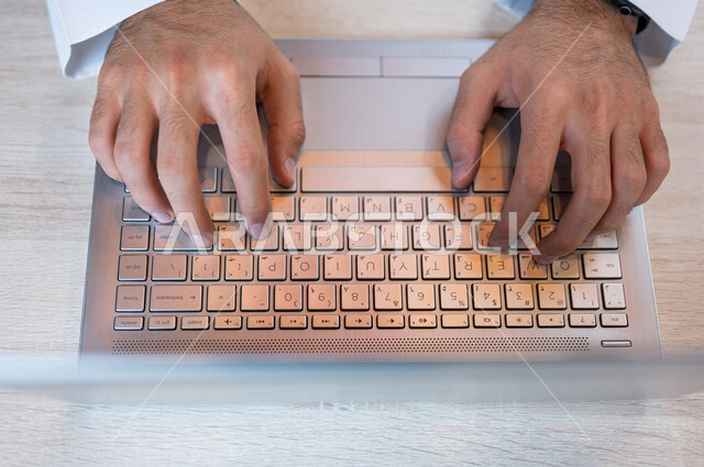 صورة مقربة ليد رجل عربي خليجي سعودي، ادارة الأعمال من خلال الحاسوب المحمول، ادخال البيانات من خلال لوحة المفاتيح، صناعة المحتويات النصية، التعليم الالكتروني