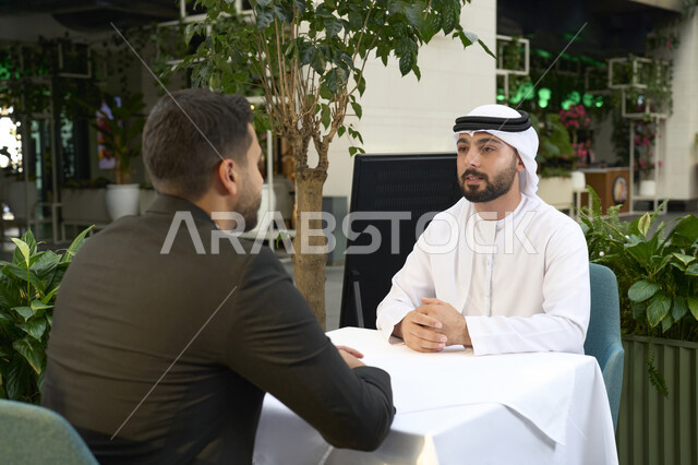 مناقشة مهام العمل، بيئة عمل اماراتي، رجل أعمال عربي إماراتي خليجي مع رجل أعمال عربي يرتدي البدلة الرسمية, الجلوس في المقهى، اجتماع زملاء عمل، الشراكة والتعاون, متابعة الأعمال وتحقيق الأهداف.