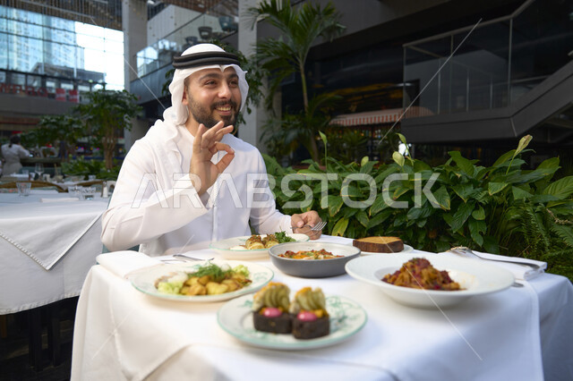 ايماءات الجودة والامتياز ، تناول الغداء في المقهى , قضاء أوقات ممتعة في المقهى، رجل عربي خليجي اماراتي يرتدي الكندورة والغترة البيضاء يجلس على مائدة الطعام ،  الاستمتاع بالأنشطة الترفيهية, مطاعم و كافيهات في الإمارات العربية المتحدة .