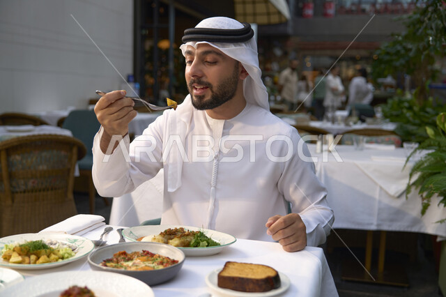 تناول الغداء في المقهى , قضاء أوقات ممتعة في المقهى، رجل عربي خليجي اماراتي يرتدي الكندورة والغترة البيضاء يجلس على مائدة الطعام ،  الاستمتاع بالأنشطة الترفيهية, مطاعم و كافيهات في الإمارات العربية المتحدة .