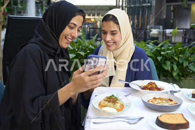 جلسة وناسة وتعارف يوم الاجازة ، التسامر والدردشة وقضاء وقت ممتع مع الأصدقاء، كوفي شوب راقي بالامارات، تعابير السعادة والسرور بلمة الرفاق، امرأتين عربيتين خليجيتين اماراتيتين تجلسان على طاولة في المقهى، تطوير العلاقات الإجتماعية، صديقتين سعوديتين تتبادلان الحديث .