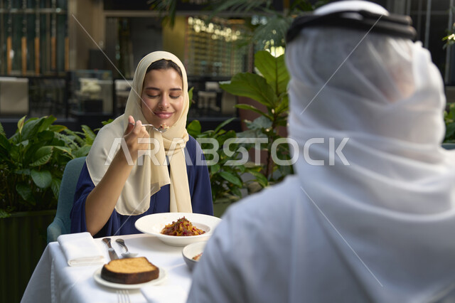 مفهوم الألفة والمحبة بين أفراد الأسرة، التسلية والترفيه بالعطلات، حوار ونقاش اسري، انشطة وفعاليات ترفيهية عائلية، ايماءات السرور والسعادة، صورة مقربة لرجل عربي خليجي اماراتي وامرأته يجلسون في المقهى يستمتعون بقضاء الوقت في الخارج .