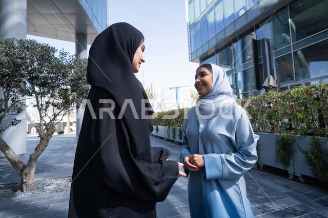تبادل الاحاديث والاخبار ، الوقوف بثقة في شوارع المدينة، الاستمتاع والتجول واستنشاق الهواء النقي في وقت النهار، صديقتان عربيتان خليجيتان سعوديتان ترتديان العباءات والحجاب ، زميلتان اماراتيان تنظران الى بعضهما بتعابير السرور، مفهوم الأناقة والاهتمام بالمظهر الخارجي .