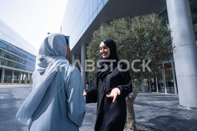 الاطمئنان على الاصدقاء ، الوقوف بثقة في شوارع المدينة، الاستمتاع والتجول واستنشاق الهواء النقي في وقت النهار، صديقتان عربيتان خليجيتان سعوديتان ترتديان العباءات والحجاب ، زميلتان اماراتيان تنظران الى بعضهما بتعابير السرور، مفهوم الأناقة والاهتمام بالمظهر الخارجي .