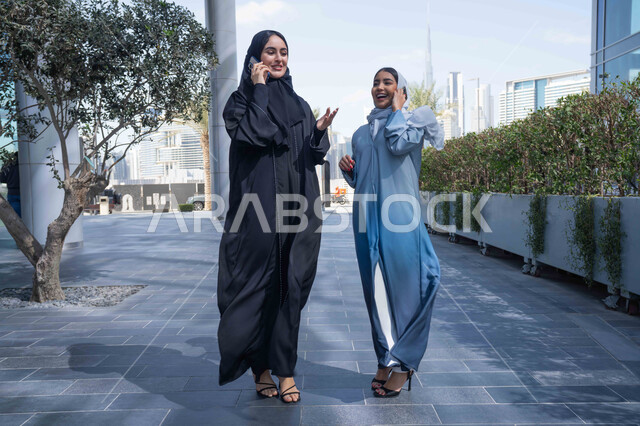التجول في إحدى المناطق العامة ، التواصل مع العائلة عبر الجوال ،الإستمتاع مع الأصدقاء, اجراء المكالمات الهاتفية ، سيدتان اماراتيان تقومان بالتنزه في وقت العطلة ، صديقتان عربيتان خليجيتان سعوديتان مبتسمتان تسيران معاً في نزهة ممتعة لإحدى الأماكن الترفيهية ، علاقات اجتماعية ، قضاء أوقات ممتعة .