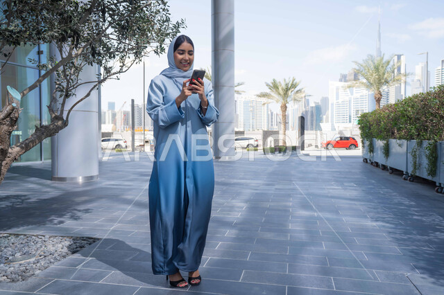 دمج الحياة مع التكنولوجيا الحديثة ، إجراء مكالمه فيديو عبر الهاتف المحمول، الدردشة والتواصل مع العائلة ، سماع الاخبار والمفاجأت السعيدة، نزهه في الهواء الطلق، إمرأة عربية خليجية اماراتية تقضي أوقات ممتعة في إحدى الحدائق في الامارات, سيدة سعودية تقوم بجولة في الطبيعة , صورة الجسم بالطول الكامل.