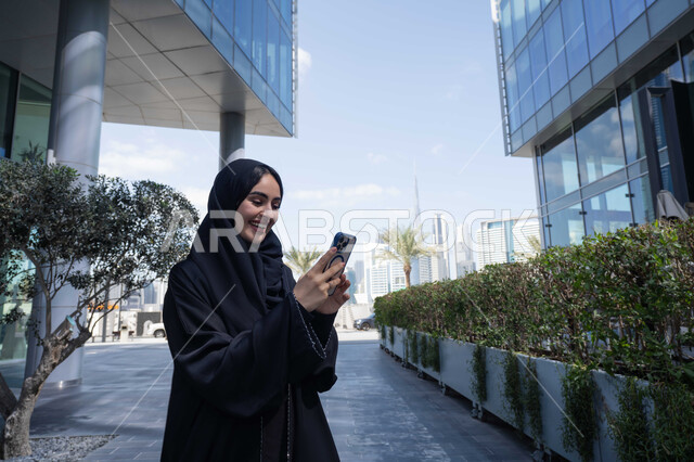 مفهوم التسويق الالكتروني عبر مواقع الاونلاين ، ايماءات السعادة لسماع الاخبار المبهجة ، برامج وتطبيقات الجوال المتنوعة ، الاطمئنان على الأصدقاء، تبادل الاحاديث والاخبار بين العائلة، امرأة اماراتية تقوم بإستخدام الأجهزة التقنية الحديثة، شابة عربية خليجية سعودية مبتسمة تمسك بيدها جهاز الهاتف المحمول .