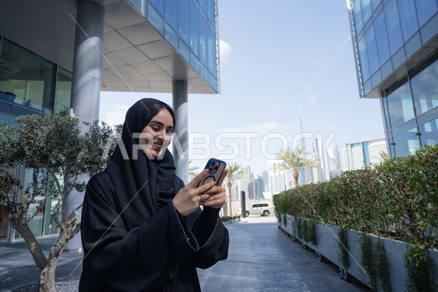 برامج وتطبيقات الجوال المتنوعة ، الاطمئنان على الأصدقاء، تبادل الاحاديث والاخبار بين العائلة، امرأة اماراتية تقوم بإستخدام الأجهزة التقنية الحديثة، شابة عربية خليجية سعودية مبتسمة تمسك بيدها جهاز الهاتف المحمول تقوم بإجراء مكالمة فيديو .