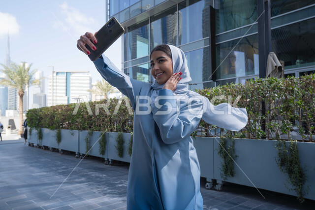 التجول في المناطق العامة, التواصل مع الأهل والأصدقاء، اجراء مكالمات الفيديو مع العائلة، توثيق اللحظات السعيدة، استخدام الهاتف المحمول والتقنيات الحديثه ، امرأة عربية خليجية سعودية ترتدي العباءة والحجاب، سيدة اماراتية تنظر بتعابير السرور تقوم باستخدام الهاتف المحمول ، نزهة  فى الهواء الطلق .