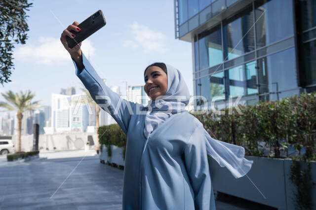 توثيق اللحظات السعيدة، استخدام الهاتف المحمول والتقنيات الحديثه، اجراء مكالمة فيديو ، امرأة عربية خليجية سعودية ترتدي العباءة والحجاب، سيدة اماراتية تنظر بتعابير السرور تقوم باستخدام الهاتف المحمول ، نزهة وجولة فى الهواء الطلق .