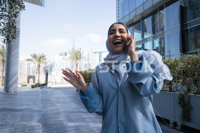 ايماءات السعادة لسماع خبر ما ، الدردشة والتواصل مع العائلة ، نزهه في الهواء الطلق، إجراء مكالمه هاتفيه عبر الهاتف المحمول، إمرأة عربية خليجية اماراتية تقضي أوقات ممتعة في إحدى الحدائق في الامارات, سيدة سعودية تقوم بجولة في الطبيعة , صورة الجسم بالطول الكامل.