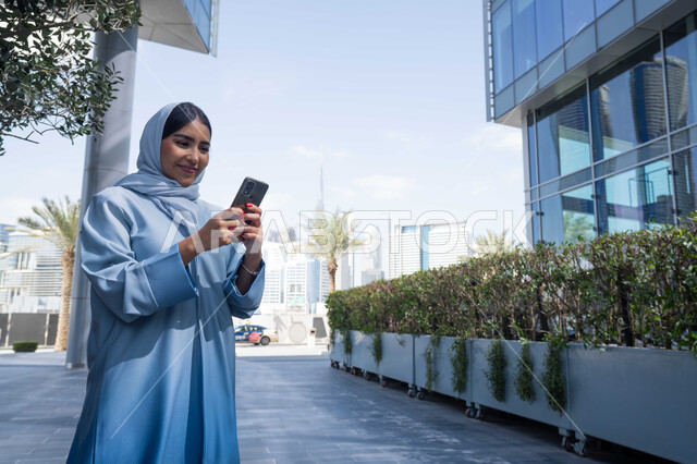 التصفح عبر مواقع الانترنت ، توثيق اللحظات السعيدة، استخدام الهاتف المحمول والتقنيات الحديثه، اجراء مكالمة فيديو ، امرأة عربية خليجية سعودية ترتدي العباءة والحجاب، سيدة اماراتية تنظر بتعابير السرور تقوم باستخدام الهاتف المحمول ، نزهة وجولة فى الهواء الطلق .