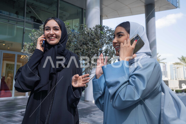 صورة مقربة لسيدتان اماراتيان تقومان بالتنزه في وقت العطلة ، التجول في إحدى المناطق العامة ، التجول برفقة  الاصدقاء ، التواصل مع العائلة عبر الجوال ، اجراء المكالمات الهاتفية ، صديقتان عربيتان خليجيتان سعوديتان مبتسمتان تسيران معاً في نزهة ممتعة لإحدى الأماكن الترفيهية ، علاقات اجتماعية .