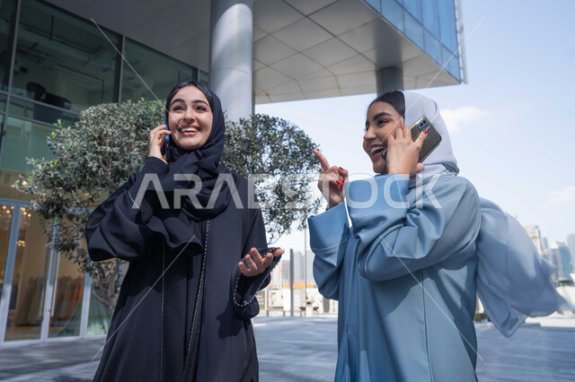 التجول برفقة  الاصدقاء ، التواصل مع العائلة عبر الجوال ، اجراء المكالمات الهاتفية ، صورة مقربة لسيدتان اماراتيان تقومان بالتنزه في وقت العطلة ، الإستمتاع مع الأصدقاء, التجول في إحدى المناطق العامة ، صديقتان عربيتان خليجيتان سعوديتان مبتسمتان تسيران معاً في نزهة ممتعة لإحدى الأماكن الترفيهية ، علاقات اجتماعية .