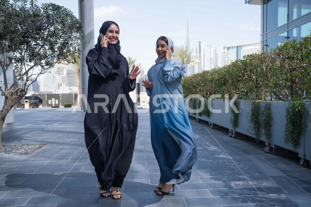 التواصل مع العائلة عبر الجوال ، اجراء المكالمات الهاتفية ، سيدتان اماراتيان تقومان بالتنزه في وقت العطلة ، الإستمتاع مع الأصدقاء,  التجول في إحدى المناطق العامة ، صديقتان عربيتان خليجيتان سعوديتان مبتسمتان تسيران معاً في نزهة ممتعة لإحدى الأماكن الترفيهية ، علاقات اجتماعية ، قضاء أوقات ممتعة .