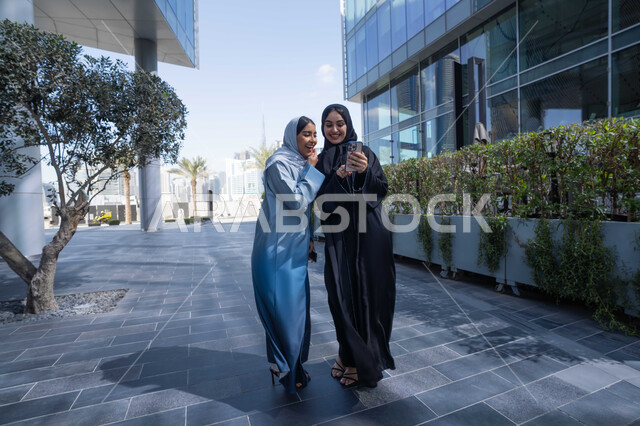 الإستمتاع مع الأصدقاء,  التجول في إحدى المناطق العامة ، صديقتان عربيتان خليجيتان سعوديتان مبتسمتان تسيران معاً في نزهة ممتعة لإحدى الأماكن الترفيهية ، سيدتان اماراتيان تقومان بالتنزه في وقت العطلة ، صداقات و تعارف ، علاقات اجتماعية ، قضاء أوقات ممتعة .