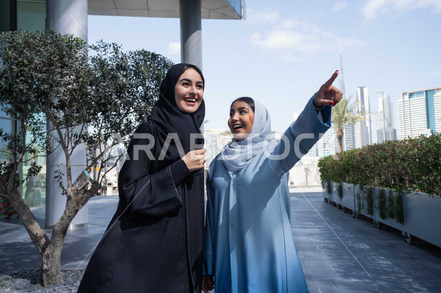 قضاء أوقات ممتعة في الطبيعة ،اشارات تحدد هذا المكان (هنا) ، تقوية وتعزيز العلاقات الاجتماعية ، صديقتان عربيتان خليجيتان سعوديتان ترتديان العباءات والحجاب، سيدتان اماراتيان تنظران الى شئ ما بتعابير السرور ، مفهوم الأناقة والاهتمام بالمظهر الخارجي ، استنشاق الهواء النقي في وقت النهار .