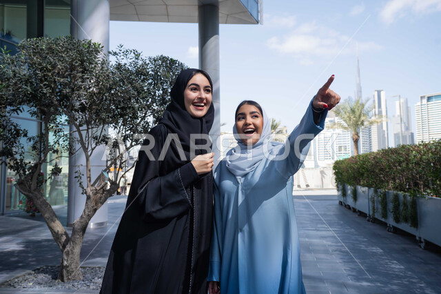 اشارات تحدد هذا المكان (هنا) ، تقوية وتعزيز العلاقات الاجتماعية ، صديقتان عربيتان خليجيتان سعوديتان محجبتان ترتديان العباءات والحجاب، قضاء أوقات ممتعة في الطبيعة ، سيدتان اماراتيان تنظران الى شئ ما بتعابير السرور ، مفهوم الأناقة والاهتمام بالمظهر الخارجي ، استنشاق الهواء النقي في وقت النهار .