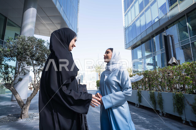 زميلتان اماراتيان تنظران الى بعضهما بتعابير السرور ، تقوية وتعزيز العلاقات الاجتماعية , الإستمتاع مع الأصدقاء, مفهوم الأناقة والاهتمام بالمظهر الخارجي ، صديقتان عربيتان خليجيتان سعوديتان محجبتان ترتديان العباءات والحجاب، قضاء أوقات ممتعة في الطبيعة ، الاستمتاع والتجول واستنشاق الهواء النقي في وقت النهار .