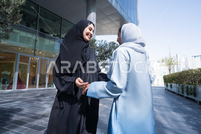 تقوية وتعزيز العلاقات الاجتماعية , الإستمتاع مع الأصدقاء, مفهوم الأناقة والاهتمام بالمظهر الخارجي ، قضاء أوقات ممتعة في الطبيعة ، الاستمتاع والتجول واستنشاق الهواء النقي في وقت النهار، صديقتان عربيتان خليجيتان سعوديتان محجبتان ترتديان العباءات والحجاب ، زميلتان اماراتيان تنظران الى بعضهما بتعابير السرور.