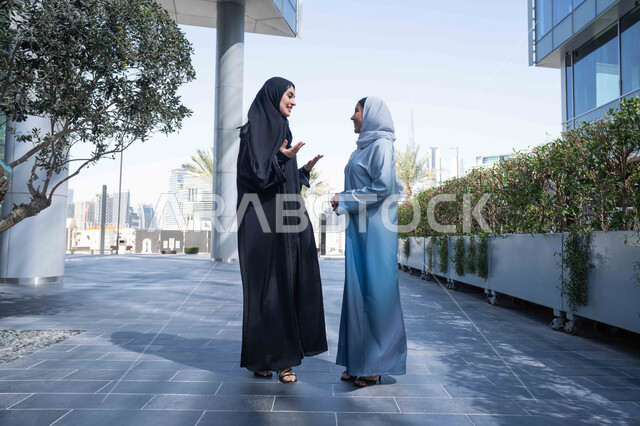 مفهوم الأناقة والاهتمام بالمظهر الخارجي ، صداقات وتعارف ونقاشات وحوارات قضاء أوقات ممتعة في الطبيعة ، الاستمتاع والتجول واستنشاق الهواء النقي في وقت النهار، صديقتان عربيتان خليجيتان سعوديتان محجبتان ترتديان العباءات والحجاب ، زميلتان اماراتيان تنظران الى بعضهما بتعابير السرور.