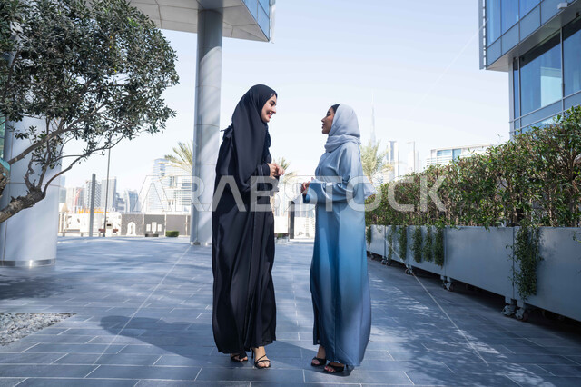 صداقات وتعارف ونقاشات وحوارات قضاء أوقات ممتعة في الطبيعة ، الاستمتاع والتجول واستنشاق الهواء النقي في وقت النهار، مفهوم الأناقة والاهتمام بالمظهر الخارجي ، صديقتان عربيتان خليجيتان سعوديتان محجبتان ترتديان العباءات والحجاب ، زميلتان اماراتيان تنظران الى بعضهما بتعابير السرور.