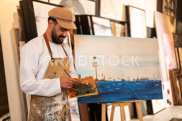 Using a brush to draw on a canvas, the concept of talent and creativity, an art workshop, an Arab Gulf Omani painter wearing a dishdasha and turban with a painting apron drawing Omani nature, passion for practicing favorite hobbies and handicrafts, expressions and gestures of integration and pleasure