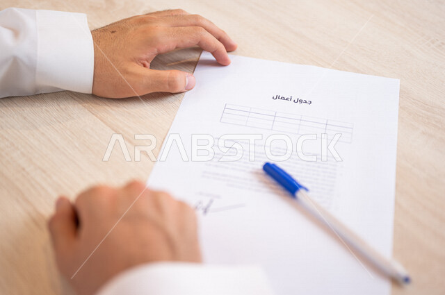 رجل عربي خليجي سعودي يسمك بيده قلم ويقوم بتجهيز جدول الأعمال، سكرتير يدير الاعمال الورقية، تنظيم جدول الاعمال والمهام، أعمال مكتبية
