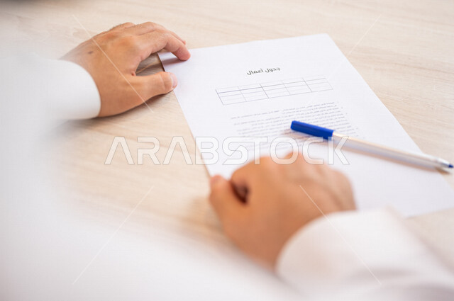 A Saudi Arabian Gulf man holding a pen in his hand and preparing the agenda, a secretary who manages paperwork, organizing the agenda and tasks, office work