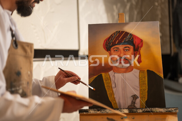 لوحة لجلالة الملك المعظم، ورشة عمل فنية, رسام عربي خليجي عماني يرتدي الدشداشة والعمامة ومريلة الرسم يقوم برسم السلطان هيثم بن طارق، الشغف في ممارسة الهوايات المفضلة والفنون اليدوية، تعابير وايماءات الاندماج والسرور، مفهوم الموهبة و الإبداع