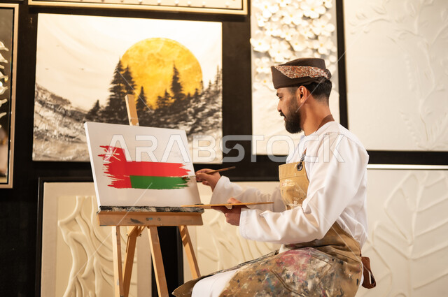 ذكرى تأسيس الدولة 1965، إحياء اليوم الوطني العماني 18 نوفمبر، ورشة عمل فنية، رسام عربي خليجي عماني يرتدي الدشداشة والعمامة مع مريلة الرسم يقوم برسم علم سلطنة عمان، ممارسة الهوايات المفضلة والفنون اليدوية، مفهوم الموهبة و الإبداع وحب الوطن والانتماء إليه