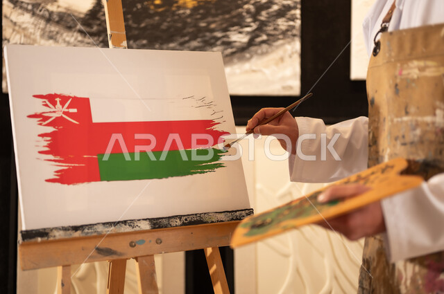 اليوم الوطني العماني 18 نوفمبر، ورشة عمل فنية، رسام عربي خليجي عماني يرتدي الدشداشة والعمامة مع مريلة الرسم يقوم برسم علم سلطنة عمان، إحياء ذكرى تأسيس الدولة 1965، ممارسة الهوايات المفضلة والفنون اليدوية، مفهوم الموهبة و الإبداع وحب الوطن والانتماء إليه