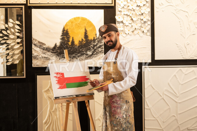 Anniversary of the founding of the state 1965, commemoration of Omani National Day November 18, art workshop, an Arab Gulf Omani artist wearing a dishdasha and turban with a painting apron drawing the flag of the Sultanate of Oman, practicing favorite hobbies and handicrafts, the concept of talent, creativity, love of the homeland and belonging to it